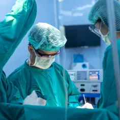 Zespół chirurgów w zielonych fartuchach i czepkach pracuje przy stole operacyjnym. Zmiana lekarza specjalisty w trakcie leczenia jest kluczowa dla powodzenia operacji.