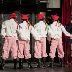 Czterech mężczyzn w strojach ludowych i kobieta w błyszczącej sukience na scenie. Zabawny moment ze spektaklu "goło i wesoło".