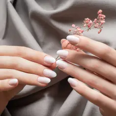 Delikatne dłonie z perfekcyjnym manicure biologicznym, trzymające gałązkę z różowymi kwiatkami.