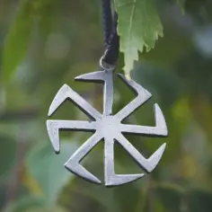 Metalowy symbol, przypominający swastykę słowiańską, wisi na tle zielonych liści.