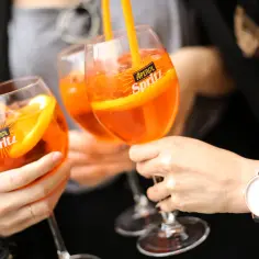 Trzy kieliszki Aperol Spritz z pomarańczą i słomką, idealne na letnie popołudnie. Tak się pije Aperol!