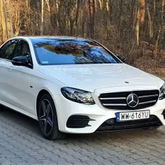 Biały Mercedes E300 z czarnym dachem i lusterkami na tle lasu.