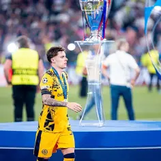 Piłkarz Nicola Zalewski, który w 2023 roku skończył 21 lat, w żółtym stroju z medalem na szyi idzie obok pucharu Ligi Mistrzów.