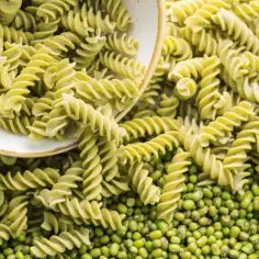 Zielone fusilli, czyli makaron z zielonego groszku, rozsypane obok świeżych ziaren groszku.