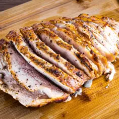 Mięciutki schab w sosie, pokrojony w plastry, leży na drewnianej desce. Aromatyczne przyprawy podkreślają smak soczystego mięsa.