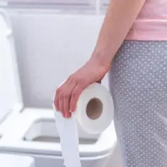 Osoba w piżamie trzymająca rolkę papieru toaletowego przy toalecie. Może szukać ulgi, np. po zastosowaniu laxigen.