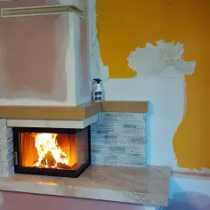 Nowa obudowa do kominka z kamienia i drewna, z palącym się ogniem. Wnętrze w trakcie remontu.