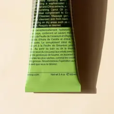 Zielony tubka z balsamem do ciała Aesop, z tekstem opisującym jego właściwości nawilżające i składniki, w tym ekstrakt z liści geranium.