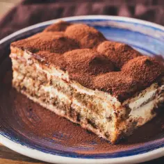 Pyszny kawałek tiramisu z mascarpone, posypany kakao, na niebieskim talerzu. Idealny na deser.