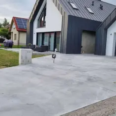 Nowy, nowoczesny dom z garażem i podjazdem z betonu szczotkowanego. Obok żółta skrzynka gazowa.