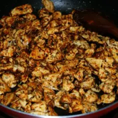 Kawałki kurczaka gyros smażą się na patelni, przyprawione ziołami i papryką.