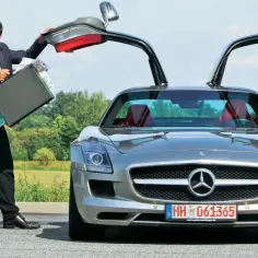 Szczęśliwy mężczyzna w garniturze otwiera drzwi swojego SLS AMG, prezentując walizkę pełną pieniędzy.