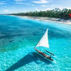 Rajska plaża na Zanzibarze, łódź z żaglem na turkusowej wodzie. Idealne miejsce na wczasy z Zanzibarem.