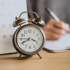 Budzik obok kalendarza z zaznaczonym 28. dniem. Zastanawiasz się, ile to godzin 1/8 etatu? Czas na planowanie!