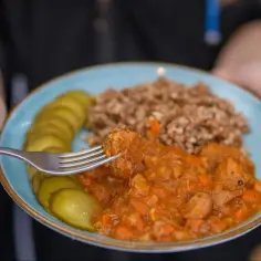 Gulasz z kaszą gryczaną, ogórki kiszone i widelec nabierający kawałek mięsa. Pyszny, sycący obiad.