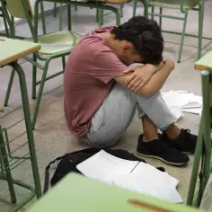 Chłopiec skulony na podłodze w pustej sali lekcyjnej, otoczony rozrzuconymi notatkami. Jego postawa wyraża głębokie niedostosowanie społeczne i poczucie osamotnienia.