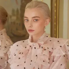 Blondynka w różowej bluzce w serduszka, z falbankami i kokardą. Jej odbicie w lustrze dopełnia charakterystykę Izabeli Łęckiej.