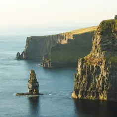 Majestatyczne klify w Irlandii, idealne na święta w Irlandii. Woda lśni, a słońce oświetla zielone zbocza i skalne iglice.