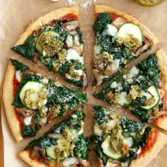 Krojona pizza ze szpinakiem, cukinią i pesto na chrupiącym spodzie.