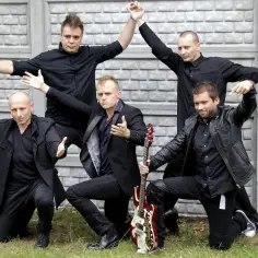 Zespół w czarnych strojach, gotowy do zagrania swoich najlepszych **coma utwory**. Jeden z nich trzyma gitarę.