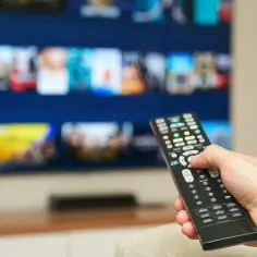 Dłoń trzymająca pilot do telewizora, na ekranie menu platformy streamingowej. Kto płaci abonament RTV w wynajmowanym mieszkaniu?