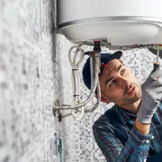 Instalator w rękawiczkach dokręca śrubę w bojlerze.