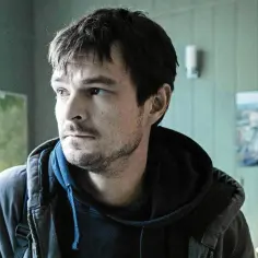 Dawid Ogrodnik w kadrze filmu, zamyślony, w tle mapa i choinka.