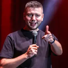 Komik z mikrofonem na scenie, wskazujący palcem. Zastanawiasz się, ile trwa stand up?