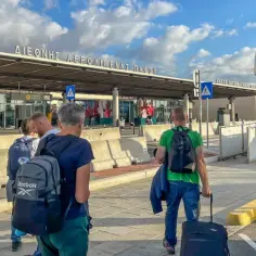 Ludzie z bagażami wychodzą z autobusu na lotnisku w Pafos. Czy na Cyprze jest bezpiecznie? Tak, podróżni bezpiecznie docierają do celu.