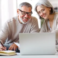 Uśmiechnięci seniorzy przy laptopie, planują przyszłość. Czy emeryt może pracować na cały etat? Oni wiedzą, że tak!