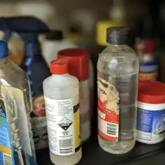 Na półce stoją różne butelki z płynami, w tym samochodowy rozpuszczalnik i płyn do mycia.
