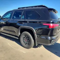 Czarny Toyota Sequoia z relingami dachowymi i terenowymi oponami stoi na placu.