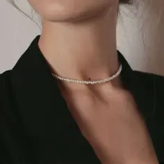 Delikatny łańcuszek z perłą, otulający szyję, dodaje elegancji czarnej marynarce.