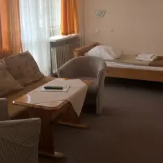 Pokój w sanatorium uzdrowiskowym „Leśnik”. Wygodna kanapa, stolik z pilotem, łóżko i krzesła.
