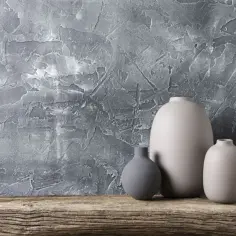 Trzy wazony na tle szarej, strukturalnej ściany i drewnianej półki.