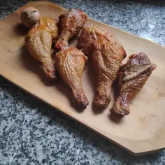 Na drewnianej desce leżą apetyczne, wędzone udka z kurczaka bez parzenia. Obok leży cebula.