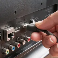 Dłoń podłącza kabel do portu HDMI ARC w telewizorze, zapewniając dźwięk przestrzenny.
