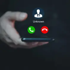 Dłoń trzyma telefon, na ekranie którego widnieje komunikat "Unknown" i przyciski odbierania/odrzucania połączenia. Brak id dzwoniącego.