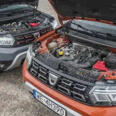 Dwa samochody Dacia z otwartymi maskami, ukazujące silnik wysokoprężny. Jeden jest szary, drugi pomarańczowy.