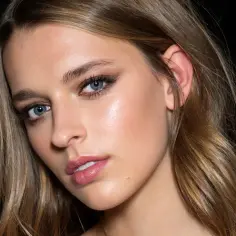 Modelka z błękitnymi oczami i subtelnym makijażem, jej włosy w odcieniu flamboyage mienią się w świetle.