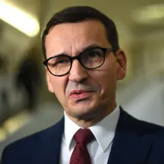 Mateusz Morawiecki w okularach i garniturze, w tle rozmyte korytarze. Dyskusja o majątku Morawieckiego trwa.