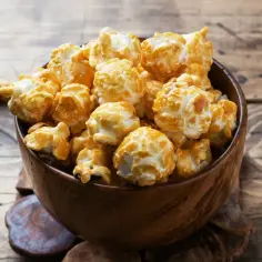 Drewniana miska pełna karmelowego popcornu na drewnianym tle.