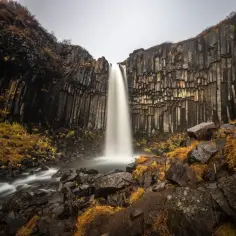 Svartifoss, najpiękniejszy wodospad, spada wśród bazaltowych kolumn. Woda tworzy mgiełkę, a jesienne barwy otaczają skały.