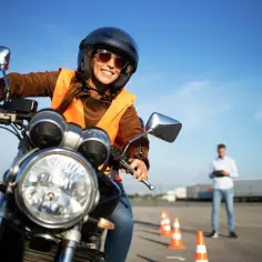 Uśmiechnięta kursantka na motorze, w kamizelce odblaskowej i kasku, uczy się jeździć. Zastanawiasz się, ile kosztuje prawo jazdy na motor?