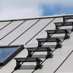 Czarne stopnie na dach do komina, zamontowane na metalowym dachu obok okna dachowego, zapewniają bezpieczne dojście.