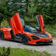 Pomarańczowy McLaren 720S z otwartymi drzwiami, zaparkowany na kamienistej drodze. Jego cena jest wysoka, ale wrażenia bezcenne.