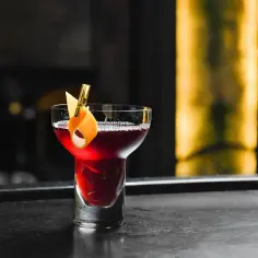 Elegancki drink czarny rusek, ozdobiony skórką pomarańczy, kusi głębokim kolorem na barze.