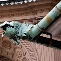 Rzygacz w kształcie smoczej głowy z zielonego metalu, odprowadzający wodę z rynny.