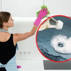 Jak doczyścić tłusty nalot na górnych szafkach kuchennych bez szorowania? Płyn z butelki tworzy pianę na blacie, a kobieta w fartuchu wyciera szafkę.