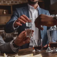 Mężczyźni w garniturach wznoszą kieliszki z alkoholem, świętując pępkowe.